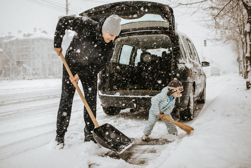 Father and little son cleaning snow around car