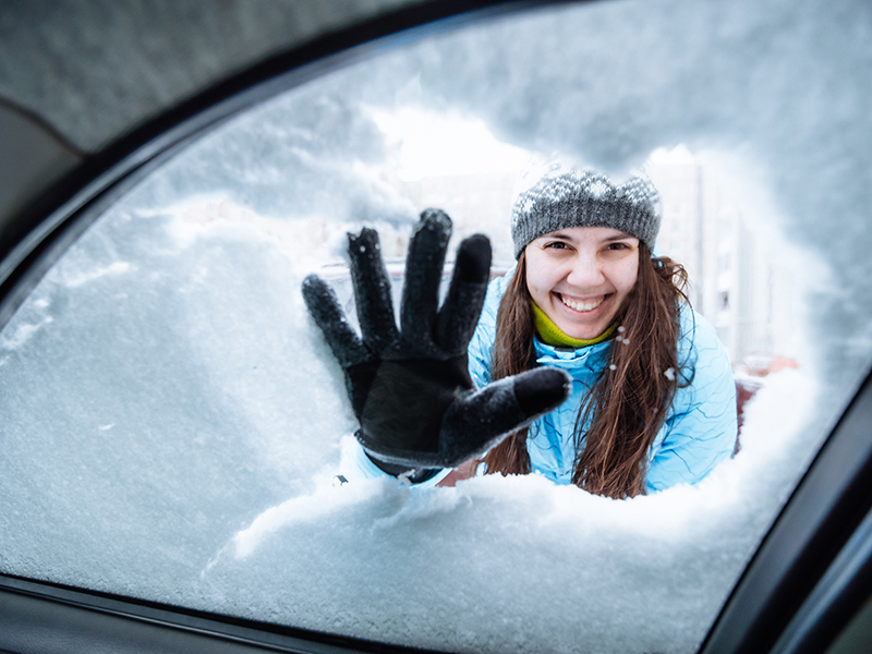 young woman clean car of snow